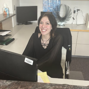 Smiling team member seated at a front desk workstation, photographed indoors for electrical team in Colorado Springs.